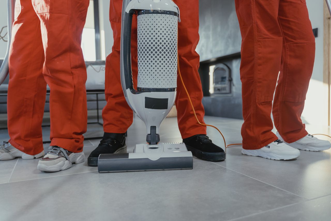 heros-img Team of professional cleaners in red uniforms using a vacuum cleaner indoors.