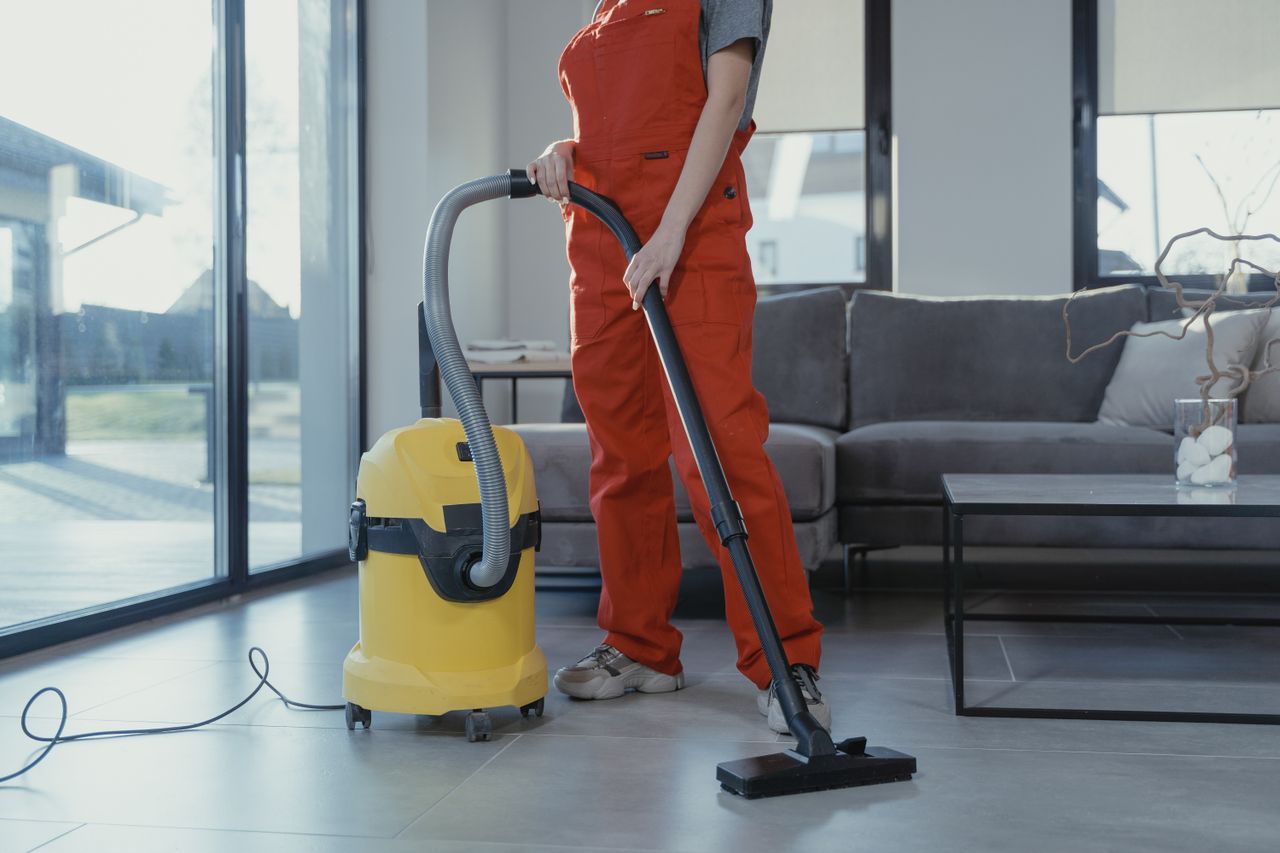 about-us-02 A professional cleaner in red coveralls vacuuming a modern living room with a yellow vacuum cleaner.